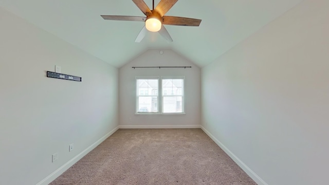 empty room with a ceiling fan, light colored carpet, vaulted ceiling, and baseboards