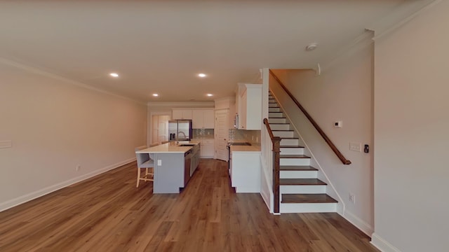 kitchen featuring a breakfast bar area, light countertops, decorative backsplash, a kitchen island with sink, and white cabinetry