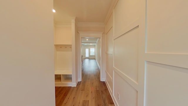 hallway featuring light wood finished floors, ornamental molding, and a decorative wall