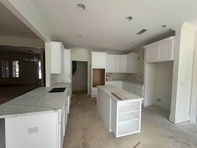 kitchen featuring light stone countertops, ornamental molding, a kitchen island, a notable chandelier, and white cabinetry