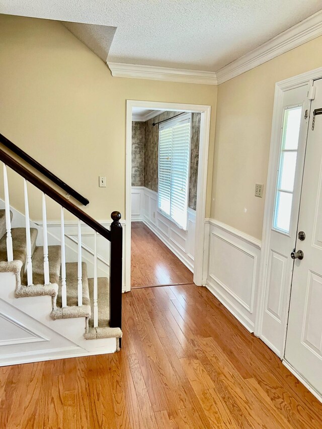 foyer entrance with plenty of natural light, wainscoting, crown molding, stairs, and a textured ceiling