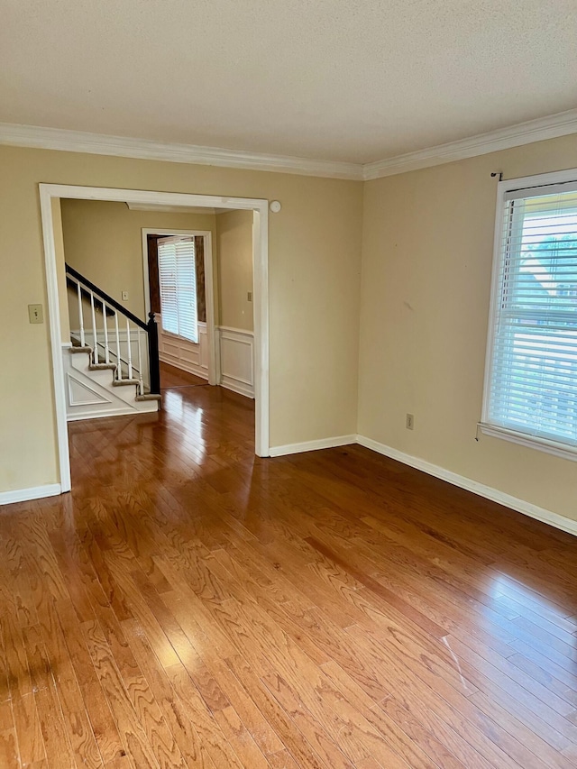 empty room featuring wood finished floors, plenty of natural light, stairway, ornamental molding, and baseboards