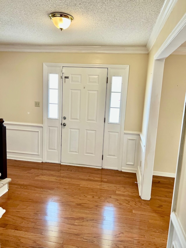 foyer featuring a textured ceiling, a wainscoted wall, hardwood / wood-style floors, ornamental molding, and a decorative wall