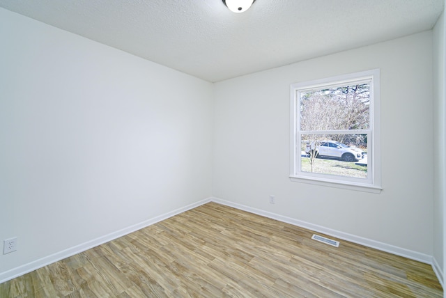 spare room with a textured ceiling and light hardwood / wood-style floors