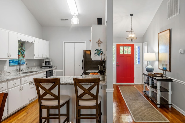 kitchen featuring a center island, refrigerator, sink, hanging light fixtures, and white cabinetry