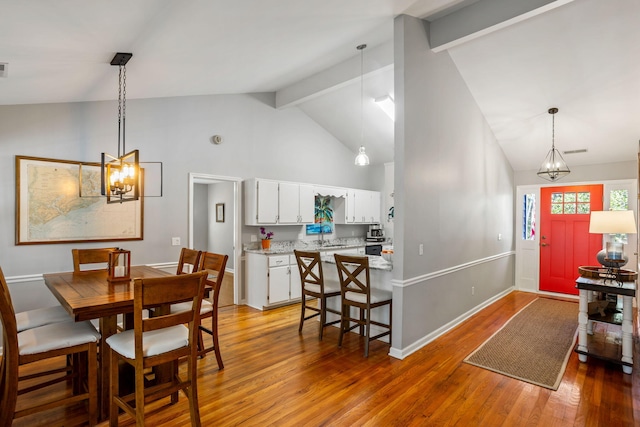 dining space featuring hardwood / wood-style flooring, beam ceiling, sink, and high vaulted ceiling