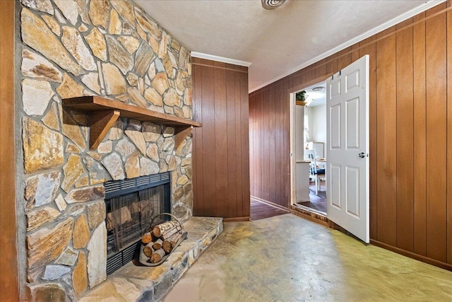 unfurnished living room with concrete flooring, a stone fireplace, wooden walls, crown molding, and a textured ceiling