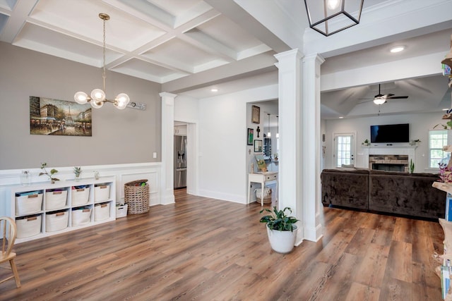 interior space featuring a fireplace, coffered ceiling, ceiling fan with notable chandelier, and decorative columns