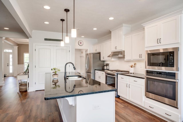 kitchen with an island with sink, appliances with stainless steel finishes, white cabinets, ornamental molding, and a sink