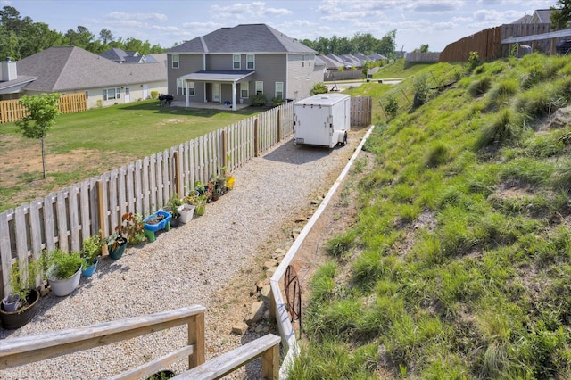 view of yard with an outdoor structure, a residential view, a storage unit, gravel driveway, and a fenced backyard