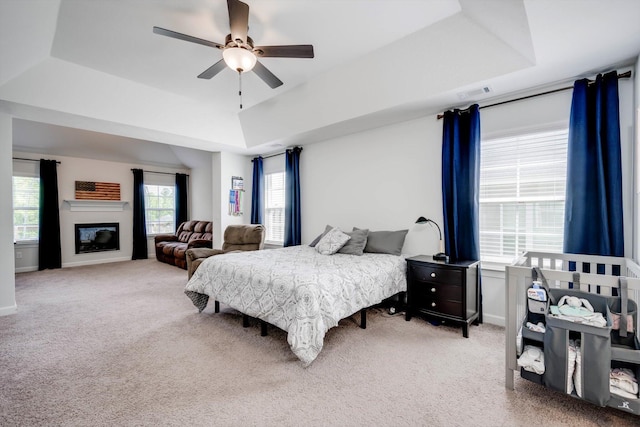 carpeted bedroom featuring ceiling fan, a glass covered fireplace, baseboards, visible vents, and a tray ceiling