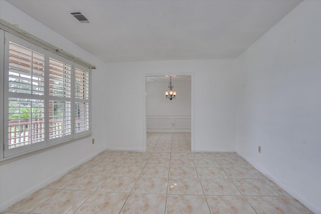 tiled spare room featuring an inviting chandelier