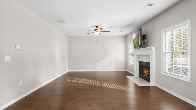 unfurnished living room featuring visible vents, baseboards, a premium fireplace, wood finished floors, and a ceiling fan