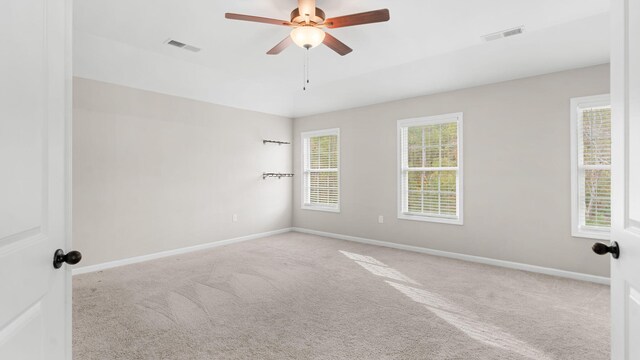 carpeted spare room featuring baseboards, visible vents, and ceiling fan