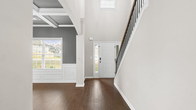 foyer entrance featuring wood finished floors, a wainscoted wall, coffered ceiling, beam ceiling, and stairs