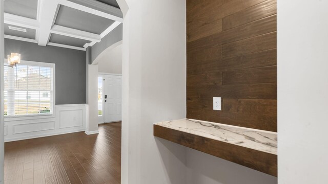 corridor featuring beamed ceiling, coffered ceiling, dark wood finished floors, arched walkways, and wainscoting