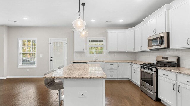 kitchen featuring dark wood-style floors, a breakfast bar, stainless steel appliances, backsplash, and a center island