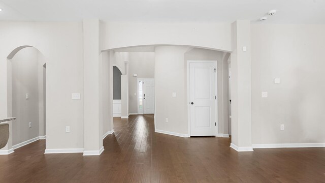 unfurnished room featuring arched walkways, vaulted ceiling, baseboards, and wood finished floors