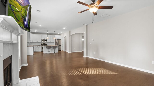 unfurnished living room with dark wood-style floors, visible vents, a ceiling fan, a fireplace with flush hearth, and arched walkways