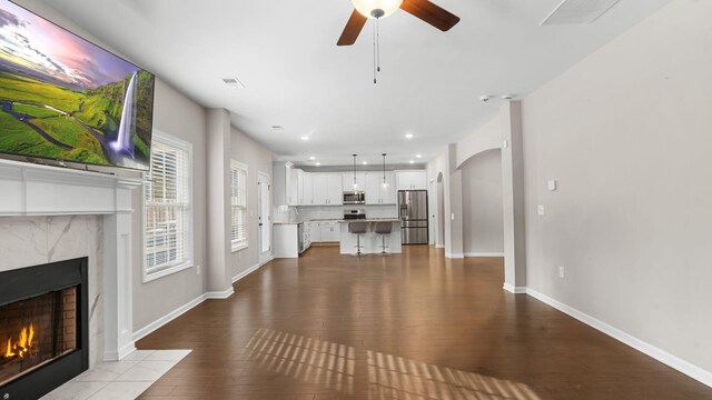 unfurnished living room with visible vents, baseboards, a premium fireplace, wood finished floors, and a ceiling fan