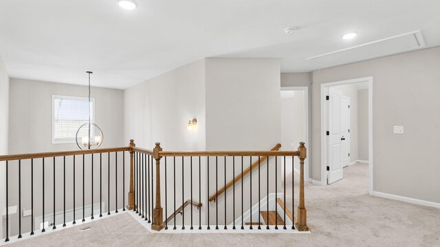 hallway featuring baseboards, carpet floors, attic access, an upstairs landing, and a chandelier