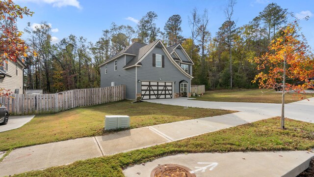 view of side of home with a yard, driveway, an attached garage, and fence