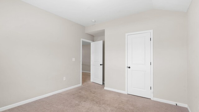 unfurnished bedroom with vaulted ceiling, light colored carpet, and baseboards