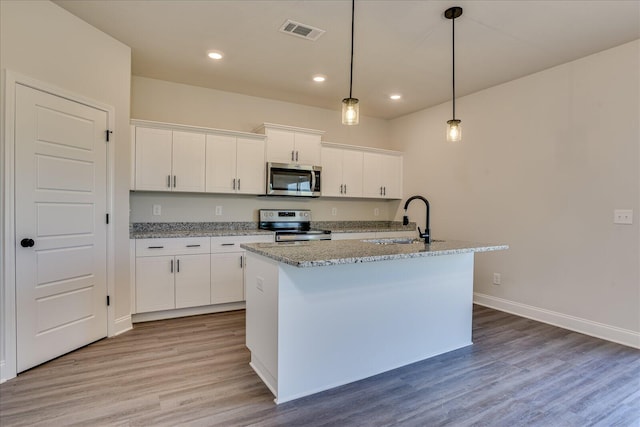 kitchen featuring appliances with stainless steel finishes, decorative light fixtures, wood-type flooring, white cabinets, and a center island with sink