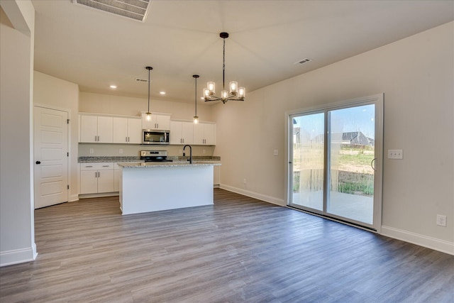 kitchen with white cabinetry, a center island with sink, hardwood / wood-style flooring, pendant lighting, and stainless steel appliances