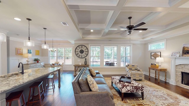 living room featuring a healthy amount of sunlight, crown molding, coffered ceiling, and sink