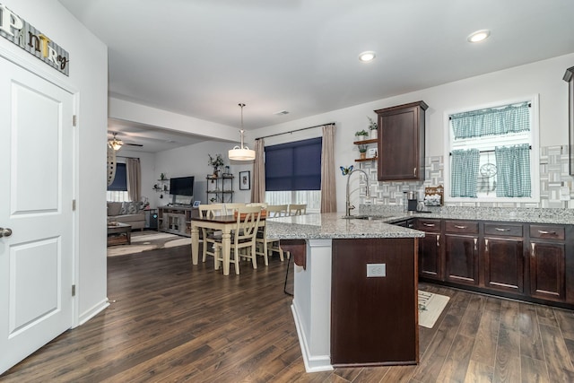 kitchen with sink, light stone counters, dark brown cabinets, dark hardwood / wood-style floors, and decorative backsplash