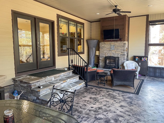 living room with ceiling fan, an outdoor stone fireplace, ornamental molding, and wooden walls