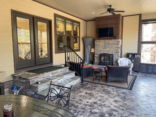 living room with ceiling fan, an outdoor stone fireplace, ornamental molding, and wooden walls