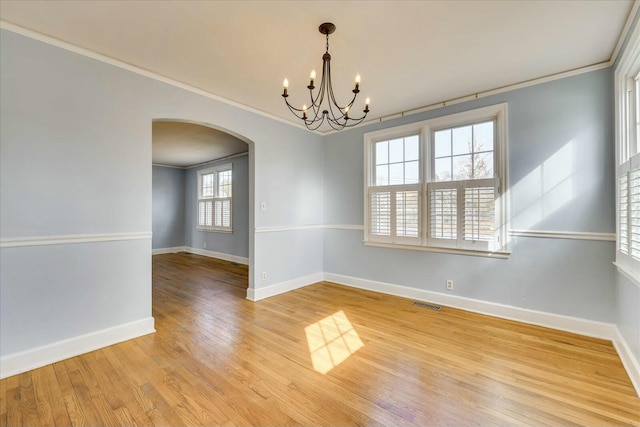 spare room featuring wood-type flooring, ornamental molding, and a chandelier