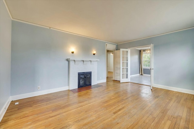 unfurnished living room featuring ornamental molding, a brick fireplace, light hardwood / wood-style floors, and french doors