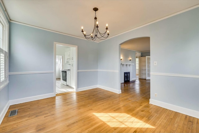 empty room with ornamental molding, a brick fireplace, a healthy amount of sunlight, and light hardwood / wood-style flooring