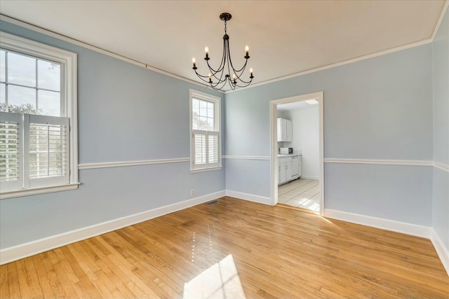 empty room featuring a notable chandelier, ornamental molding, and light wood-type flooring