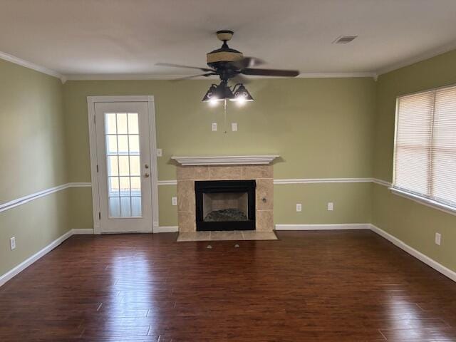 unfurnished living room with a tiled fireplace, crown molding, dark hardwood / wood-style floors, and ceiling fan