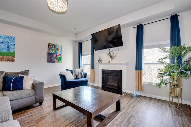 living room featuring a fireplace with flush hearth, visible vents, baseboards, and wood finished floors