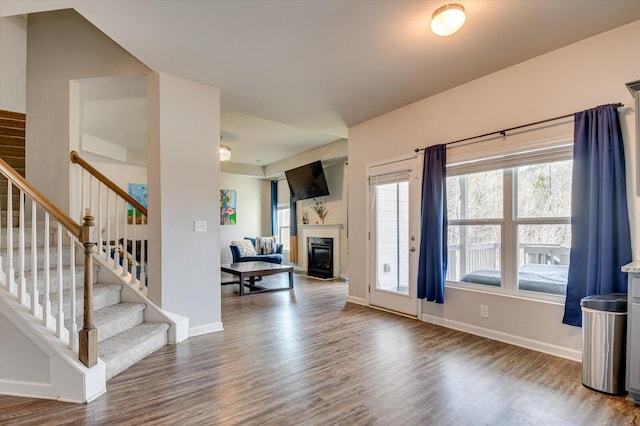 entrance foyer with stairs, a glass covered fireplace, wood finished floors, and baseboards