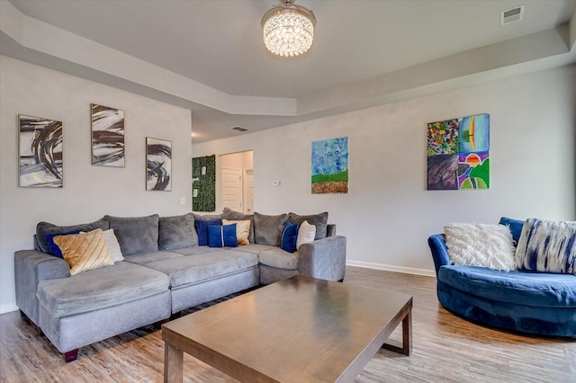 living area featuring baseboards, visible vents, a raised ceiling, and wood finished floors