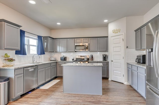 kitchen featuring appliances with stainless steel finishes, a center island, light stone countertops, gray cabinets, and a sink