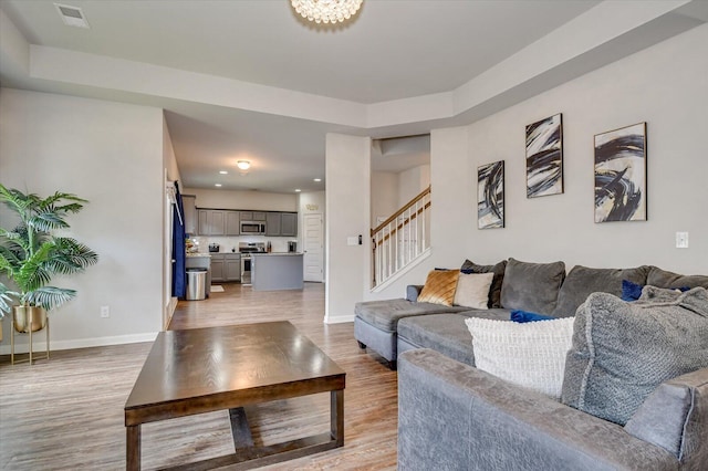 living area with baseboards, stairway, visible vents, and light wood-style floors