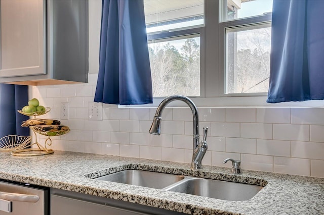 kitchen featuring a sink, backsplash, stainless steel dishwasher, and light stone countertops