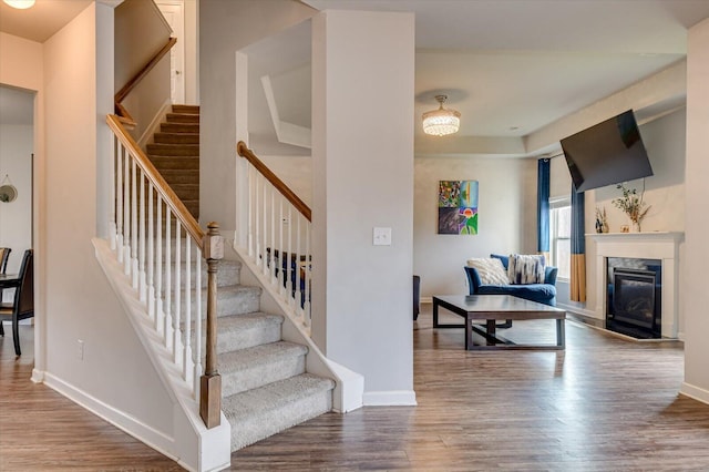 stairs with wood finished floors, a high end fireplace, and baseboards