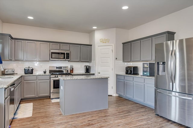 kitchen with light stone counters, light wood finished floors, stainless steel appliances, a sink, and a kitchen island