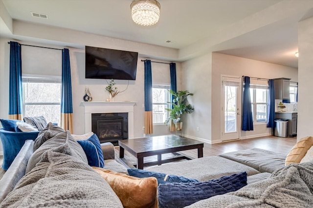 living area featuring light wood finished floors, plenty of natural light, visible vents, and a glass covered fireplace