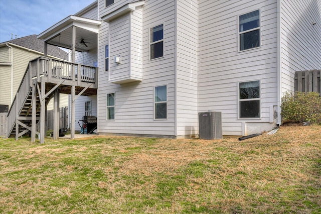 rear view of property with cooling unit, ceiling fan, stairway, and a lawn