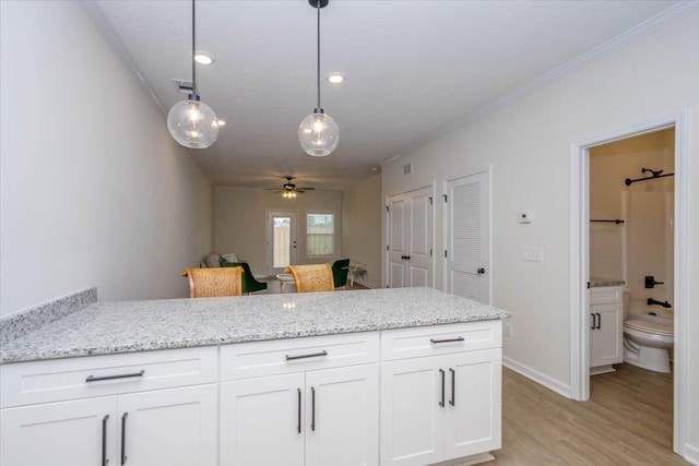 kitchen featuring pendant lighting, white cabinets, crown molding, light stone countertops, and light hardwood / wood-style flooring