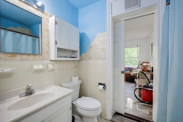full bath featuring visible vents, vanity, toilet, and tile walls